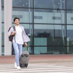 Happy millennial guy going out of airport building