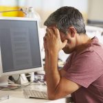 Stressed Man Working At Desk In Busy Creative Office