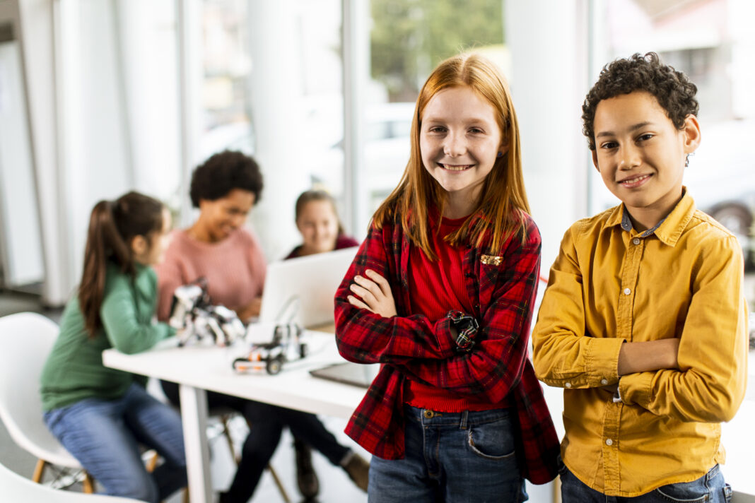 Best friends standing in front of kids programming electric toys